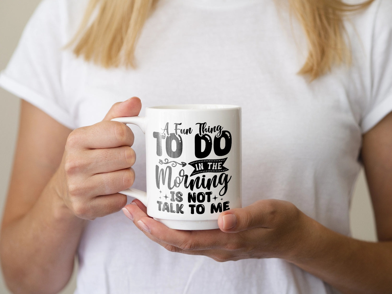 Eine Person in einem weißen Hemd hält eine weiße Tasse mit schwarzem Text, auf dem steht: „Eine lustige Sache, die man morgens machen kann, ist, nicht mit mir zu reden.“.