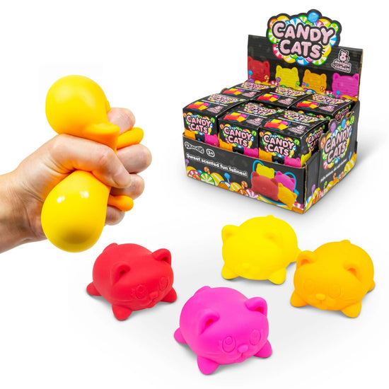 Eine Hand drückt ein gelbes, katzenförmiges Squishy-Spielzeug der Marke Candy Cats von www.buyon.at. Im Hintergrund sind in einem Kartondisplay mit der Aufschrift „Candy Cats“ weitere Squishy-Katzenspielzeuge in verschiedenen Farben (rot, gelb und pink) übersichtlich präsentiert – perfekt für Fans von Trendspielzeuge.