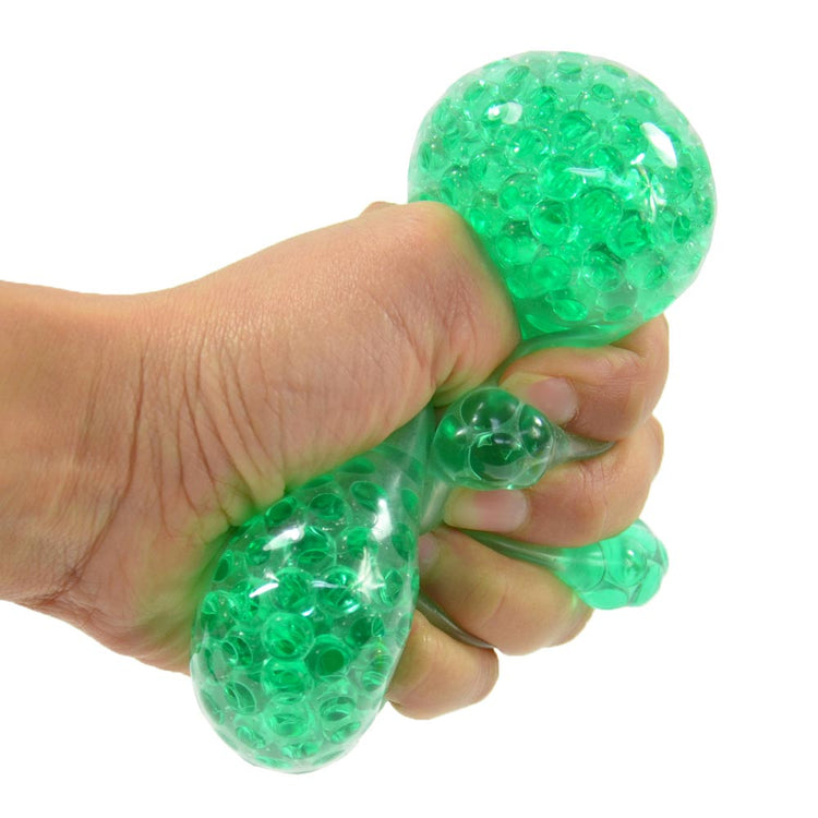 Eine Hand drückt einen grünen, transparenten Crystal Beads Ball von www.buyon.at, der mit gelartigen Perlen gefüllt ist. Der 7 cm große Stressball hat eine bauchige Form mit nach außen ragenden kleineren Abschnitten, und die Perlen im Inneren sind sichtbar und bewegen sich, wenn der Ball zusammengedrückt wird, was für einen effektiven Stressabbau sorgt.