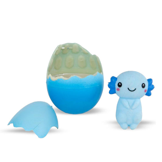 Ein süßes, blaues Axolotl-Spielzeug von www.buyon.at steht neben einem gesprungenen blau-weißen Ei mit wachsendem Axolotl 6cm. Das Ei hat zwei große Schalenstücke auf dem Boden, die verraten, wo das Spielzeug aufgetaucht ist. Der Axolotl hat ein lächelndes Gesicht und kleine, rosa Kiemen an den Seiten seines Kopfes.