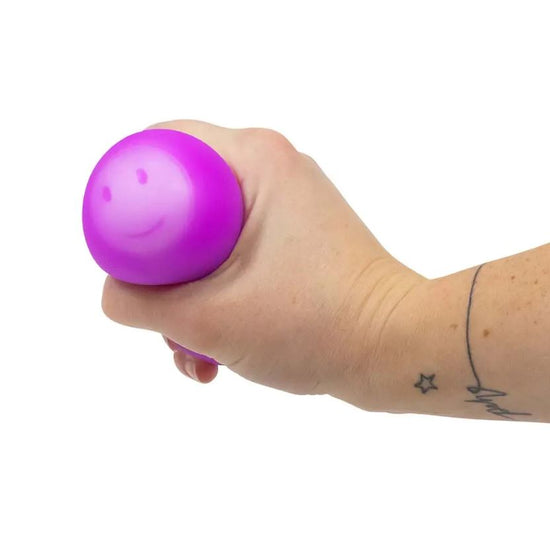 Eine Hand mit einem Sternentattoo am Handgelenk drückt einen lila Emotions Squish Ball von www.buyon.at, der mit einem Smiley bedruckt ist und so für eine angenehme sensorische Stimulation sorgt. Der Hintergrund ist schlicht weiß.