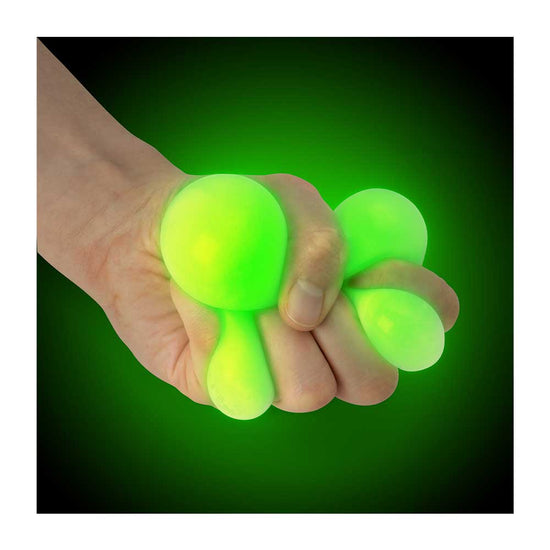 Eine Hand drückt einen im Dunkeln leuchtenden Squish Ball von www.buyon.at, der aus mehreren prall gefüllten Segmenten besteht, vor einem dunkelgrünen und schwarzen Farbverlaufshintergrund. Der Stressball ist hell beleuchtet, wodurch ein lebhafter Neoneffekt entsteht, was ihn zu einem perfekten Zappel- und Sensorikspielzeug macht.