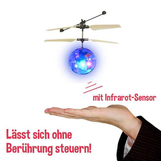 Ein kleines Flugspielzeug mit rotierenden Blättern, der Helicopter Ball mit Licht von www.buyon.at, schwebt über einer offenen Hand und bietet ein interaktives Flugerlebnis. Das Spielzeug verfügt über farbenfrohe LED-Lichteffekte und einen Hinweis auf einen Infrarotsensor. Der deutsche Text lautet: „Lässt sich ohne Berührung steuern!“ und „mit Infrarot-Sensor“ für berührungslose Bedienung.