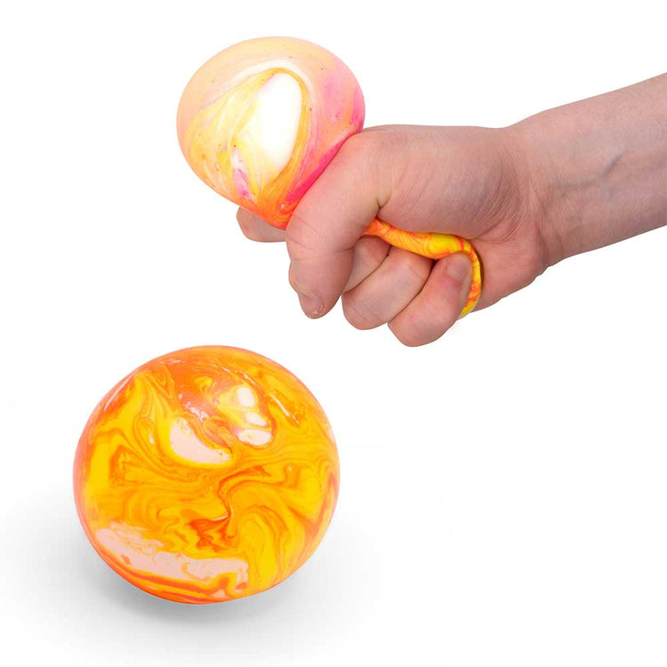 Eine Hand drückt einen Marble Squish Ball von www.buyon.at, der ein gelb-oranges Marmormuster aufweist, das eine weiße Mitte freigibt. Ein weiterer Ball mit dem gleichen Marmoreffekt-Design liegt darunter und bietet hervorragende taktile Stimulation.