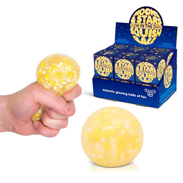 Eine Hand drückt einen gelben Squish Ball von Moons & Stars, der mit weißen Sternen und Monden verziert ist und im Dunkeln leuchtet. Ein weiterer Ball liegt auf einer Oberfläche in der Nähe. Auf der Verpackung im Hintergrund steht „Squish Ball von Moons & Stars, der im Dunkeln leuchtet“ und wird in einer blauen Schachtel von www.buyon.at präsentiert. Perfekt, um Ihrer täglichen Stressbewältigungsroutine ein Zappelelement hinzuzufügen.
