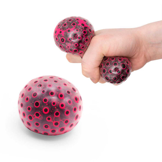 Eine Hand drückt zwei kleine, runde Stressbälle mit schwarz-rosa Pünktchenmuster. Auf der Fläche im Vordergrund liegt ein weiterer großer Neon Beans Squeeze Ball von www.buyon.at mit gleichem Motiv.