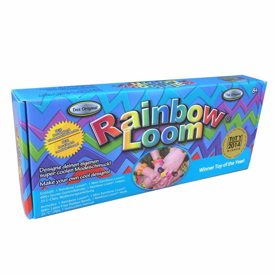 Die farbenfrohe Verpackung des Original Rainbow Loom Starter-Sets von www.buyon.at ist mit einem lebhaften Zickzack-Muster im Hintergrund versehen. In der Mitte steht prominent der Text „Rainbow Loom“. Auf dem Schild ist ein „Gewinnerspielzeug des Jahres 2014“-Abzeichen mit Angaben zum Inhalt zu sehen: Gummibänder, C-Clips, Webstuhl und Haken.