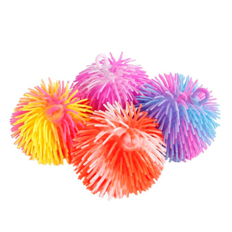 Eine Sammlung von vier farbenfrohen Pufferbällen von www.buyon.at wird ausgestellt. Jeder Ball besteht aus weichen, gummiartigen Fasern in verschiedenen Farben – Gelb, Rosa, Lila, Orange und Blau. Die strukturierte Oberfläche verstärkt das taktile Erlebnis. Die Bälle sind dicht beieinander auf einem weißen Hintergrund angeordnet.
