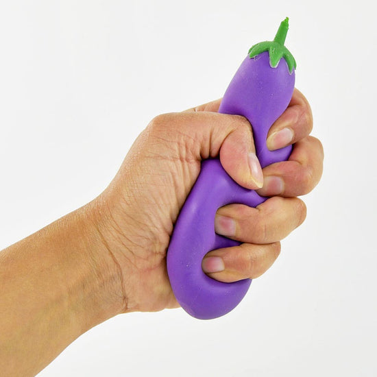 Eine Hand drückt ein Quetsch-Aubergine-Stressspielzeug von www.buyon.at, das die Form einer violetten Aubergine mit grünem Deckel hat, vor einem schlichten weißen Hintergrund. Dieses Spielzeug für Kinder ist perfekt zum Stressabbau und macht allen Altersgruppen Spaß.