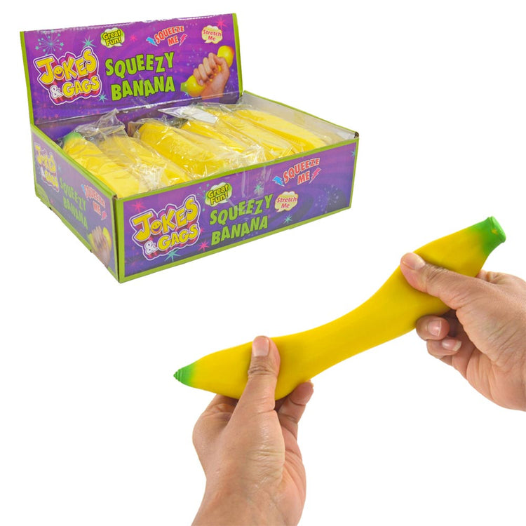 In einer Schachtel mit der Aufschrift „www.buyon.at Squeeze Banane“ sind mehrere Spielzeugbananen zu finden. Vorne strecken zwei Hände eines der leuchtend gelben Squeeze Banane-Stressspielzeuge aus, das an beiden Enden grüne Spitzen hat. Der Hintergrund ist weiß.