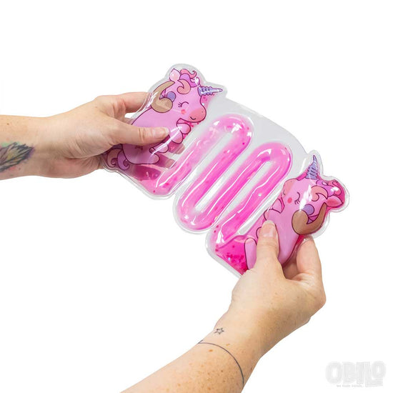 Zwei Hände halten das süße Sensorik Spielzeug Einhorn von www.buyon.at. Dieses bezaubernde rosa Gelpack mit Einhornmotiv ist mit rosa Gel gefüllt und mit verspielten Einhorn-Illustrationen verziert, was es ideal für taktiles Spielen macht. Die Person, die das Pack hält, hat ein kleines Tattoo am rechten Handgelenk.