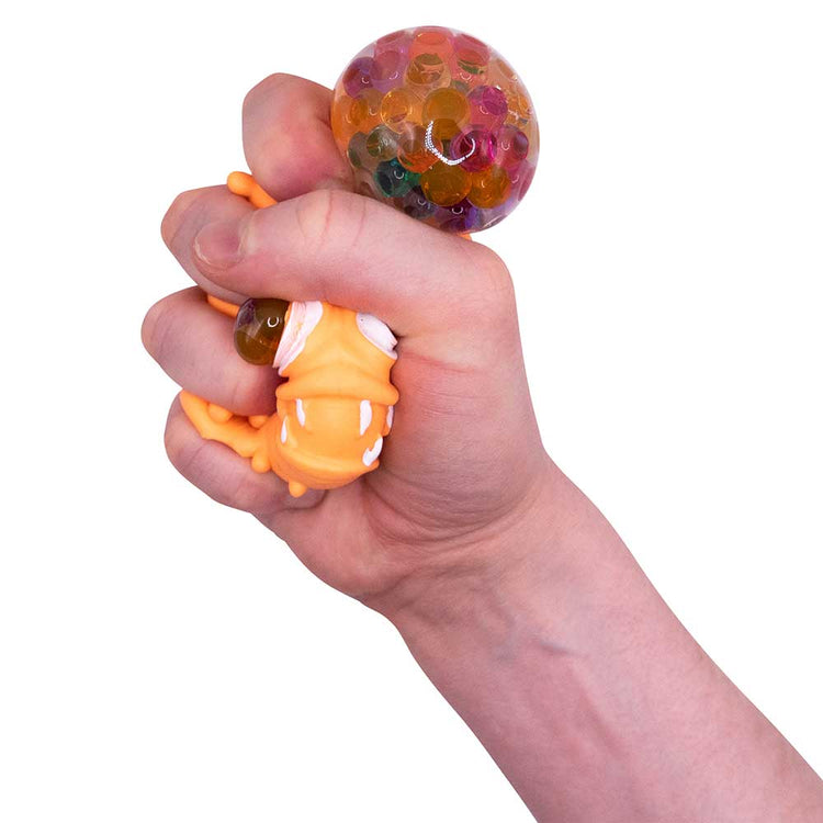 Eine Hand drückt einen Stressball in Entenform, Teil der Squeeze Monster Face-Kollektion von www.buyon.at, gefüllt mit bunten Gelperlen. Die transparente Blase an der Oberseite gibt den Blick auf bunte Perlen im Inneren frei, und der Kopf der Ente ist gequetscht und ragt aus dem Griff heraus. Ideal für alle, die Stress abbauen müssen.