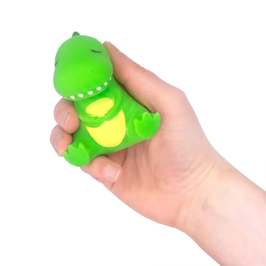 Eine Hand hält ein kleines, grünes Dinosaurier-Stressspielzeug mit gelben Details auf dem Bauch. Das Spielzeug, genannt Stretchy Sleepy Dino von www.buyon.at, hat ein lächelndes Gesicht und wirkt weich und quetschbar. Dieses einzigartige Spielzeug hilft beim Stressabbau. Der Hintergrund ist weiß.