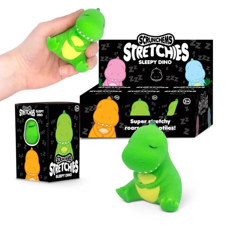 Eine Person quetscht ein kleines, grünes Stretchy Sleepy Dino-Spielzeug in ihrer Hand. Hinter der Hand befinden sich eine Schachtel und eine Auslage mit ähnlichen Spielzeugen mit der Aufschrift „Stretchy Sleepy Dino“. Das dehnbare, stressabbauende Spielzeug von www.buyon.at hat geschlossene Augen. An der Seite ist auch ein verpacktes Spielzeug zu sehen.