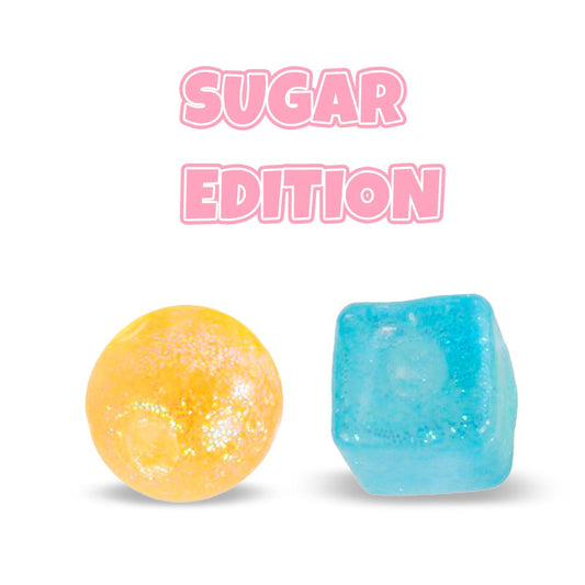 Unter dem fettgedruckten rosafarbenen Text „SUGAR EDITION“ befinden sich zwei leuchtende Bonbons. Eines ist eine glitzernde gelbe Kugel, die an einen Sugar Mellow Glitter Quetschball von www.buyon.at erinnert, und das andere ist ein glänzender blauer Würfel, beide vor einem makellos weißen Hintergrund.