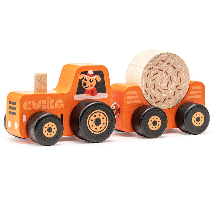 Ein Holzspielzeugtraktor mit abnehmbarem, magnetisch befestigtem Anhänger, beide orange lackiert mit runden schwarzen Rädern. Dieser Holzspielzeug Traktor mit Heuballen von www.buyon.at zeigt an der Seite ein lächelndes Hundebild mit Hut. Der Anhänger transportiert einen großen zylindrischen Heuballen aus Holz.